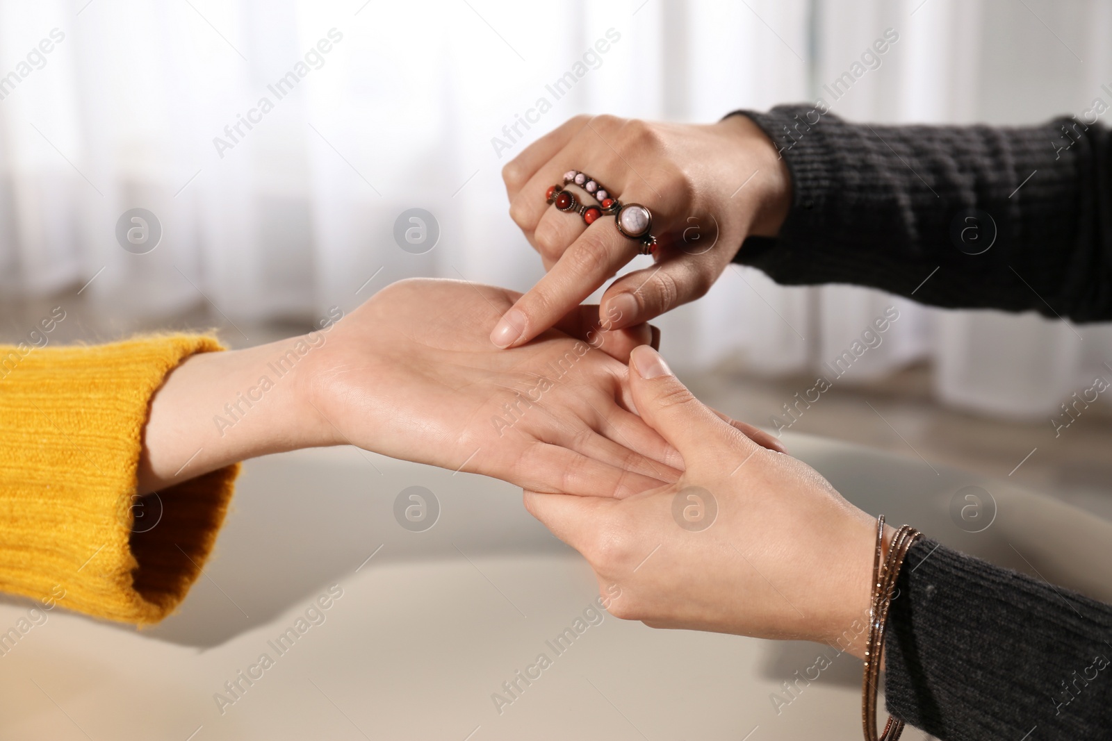 Photo of Chiromancer reading lines on woman's palm at table, closeup