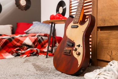 Photo of Stylish guitar and red headphones on wooden table in teenager's room