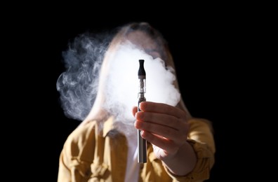 Young woman holding electronic cigarette against black background, focus on hand