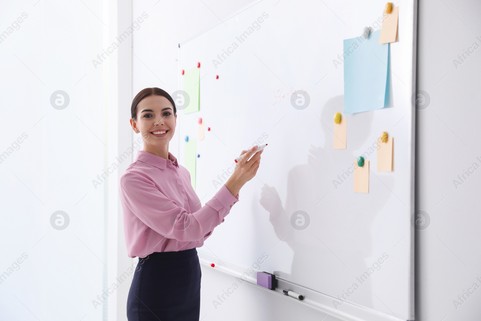 Photo of Young teacher writing on whiteboard in classroom