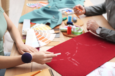 Photo of Fashion designers creating new clothes at table in studio, closeup