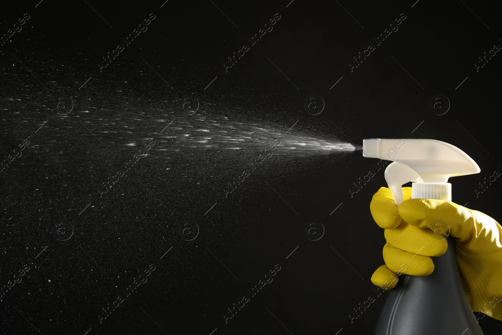 Photo of Woman spraying liquid from bottle on black background, closeup