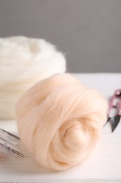 Photo of Felting wool and needles on white wooden table, closeup