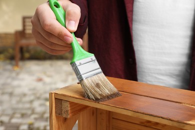 Photo of Man applying wood stain onto crate outdoors, closeup