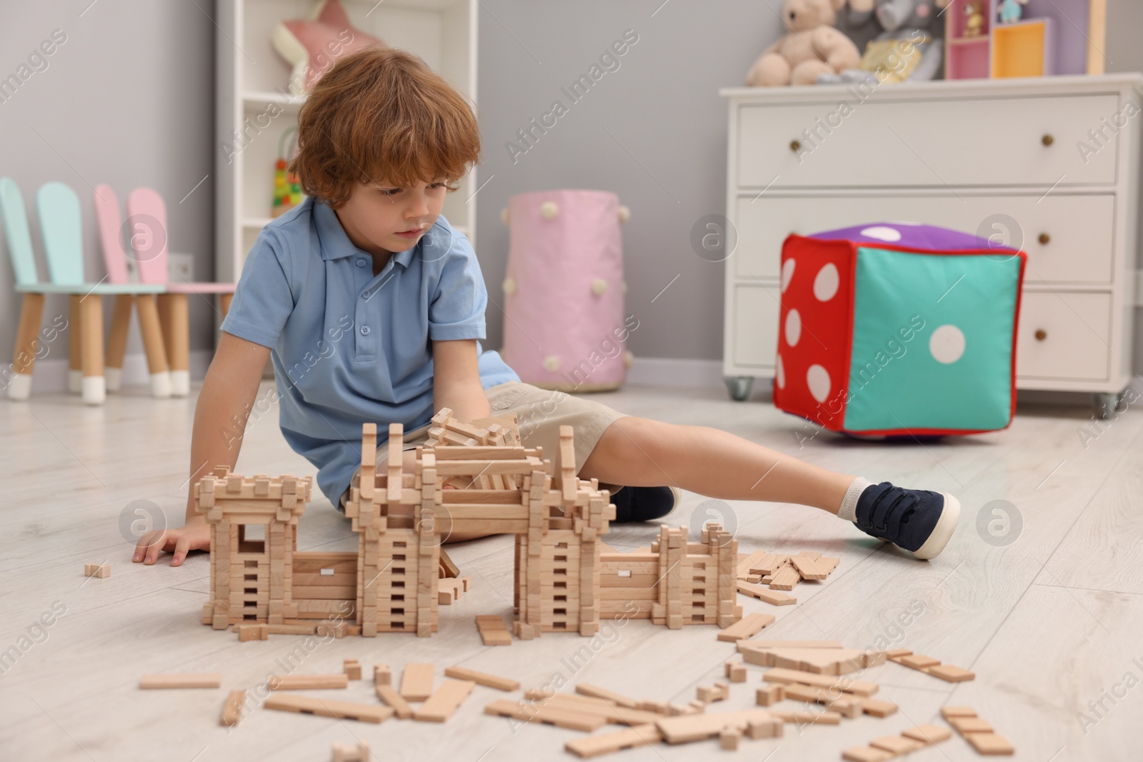 Photo of Little boy playing with wooden construction set on floor in room. Child's toy