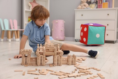 Photo of Little boy playing with wooden construction set on floor in room. Child's toy