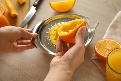 Photo of Woman squeezing orange juice at wooden table, closeup