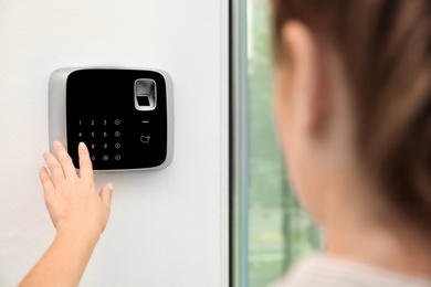 Young woman entering code on alarm system keypad indoors