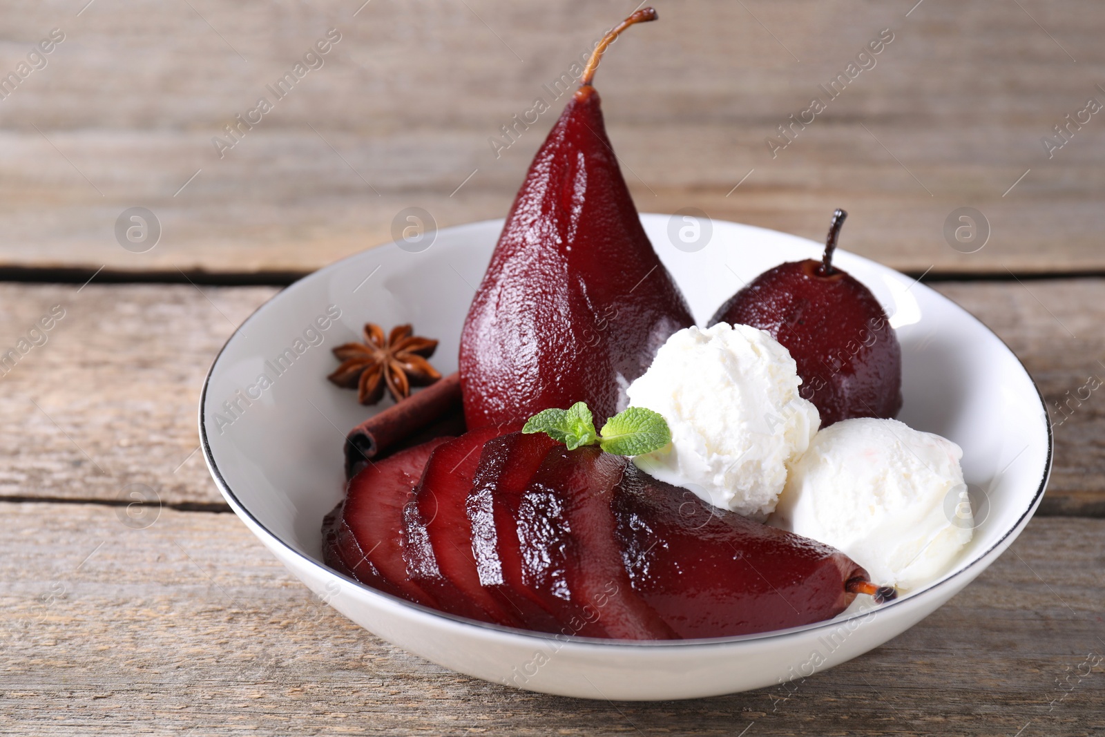 Photo of Tasty red wine poached pears and ice cream in bowl on wooden table, closeup