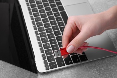 Woman holding USB cable near laptop at grey table, closeup