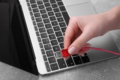 Photo of Woman holding USB cable near laptop at grey table, closeup