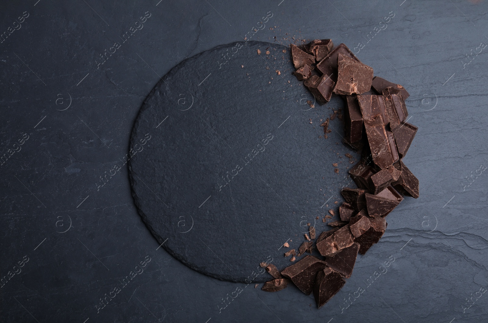 Photo of Pieces of dark chocolate and slate plate on black table, flat lay. Space for text