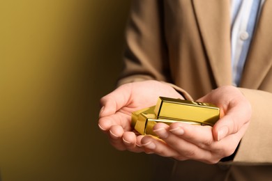 Woman holding shiny gold bars on yellow background, closeup. Space for text