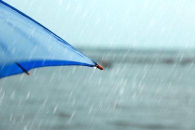 Blue umbrella under rain near river, closeup view