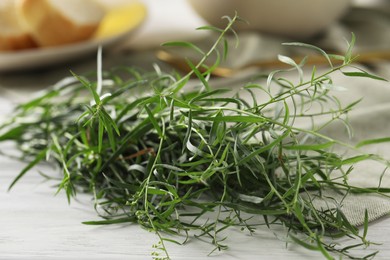 Photo of Fresh tarragon sprigs on white wooden table, closeup