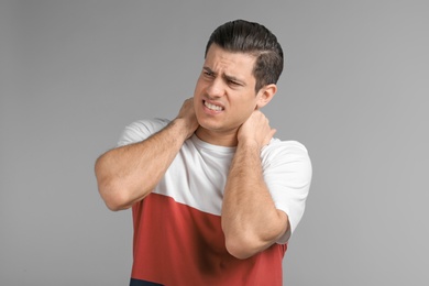 Young man suffering from neck pain on grey background