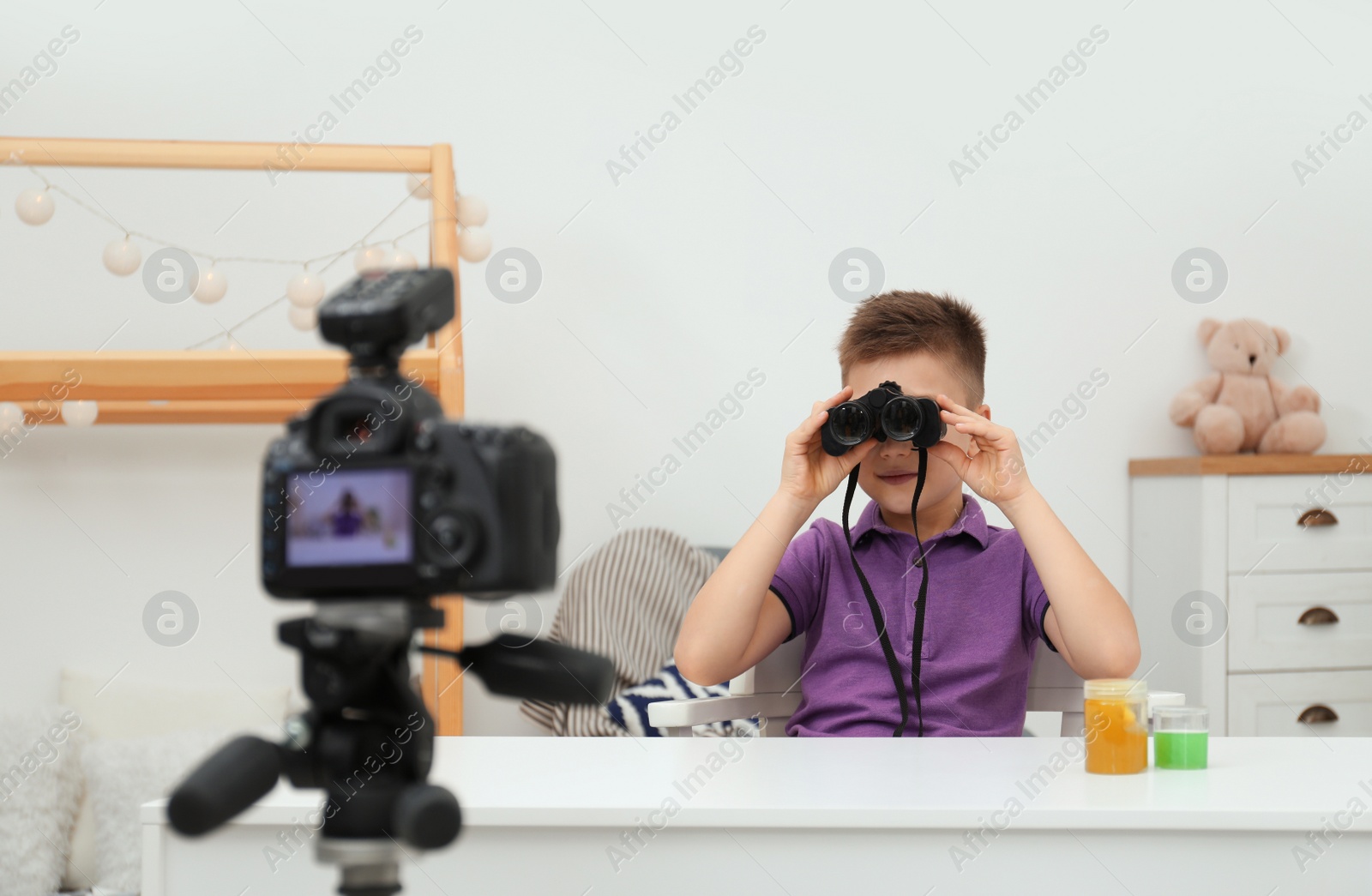 Photo of Cute little blogger with binoculars recording video at home