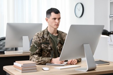 Photo of Military education. Young student in soldier uniform learning at wooden table in room