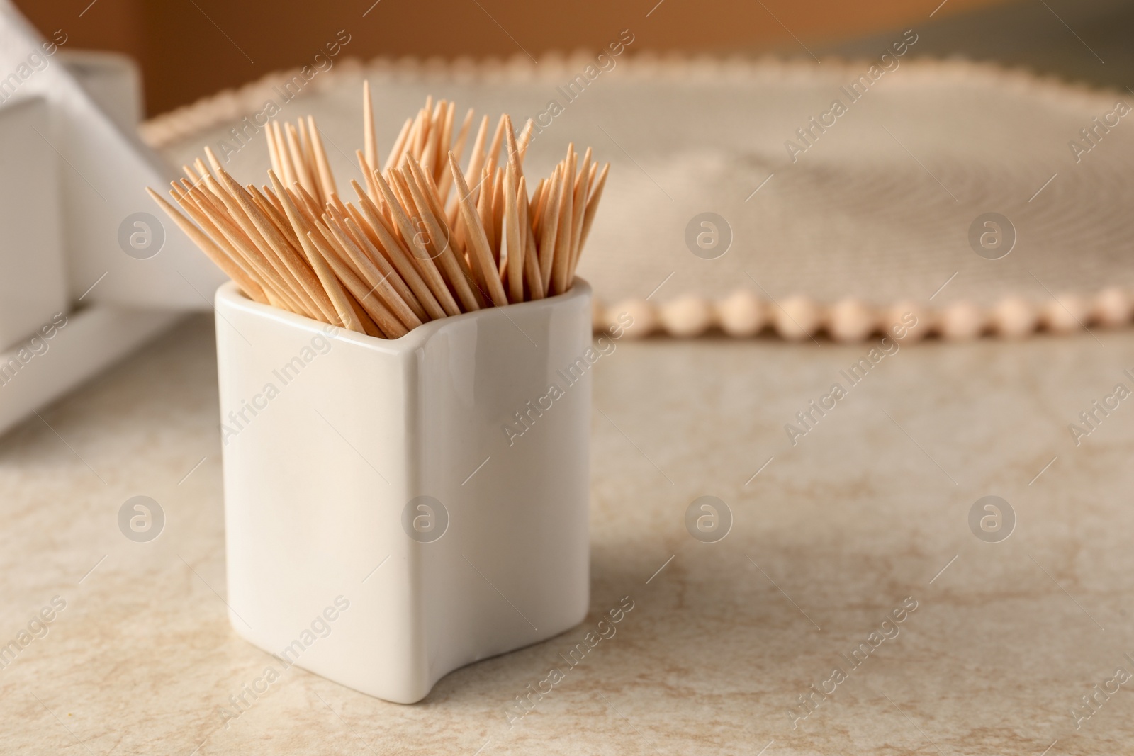 Photo of Holder with many toothpicks on beige table, closeup. Space for text