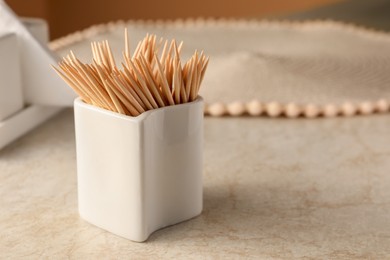 Photo of Holder with many toothpicks on beige table, closeup. Space for text