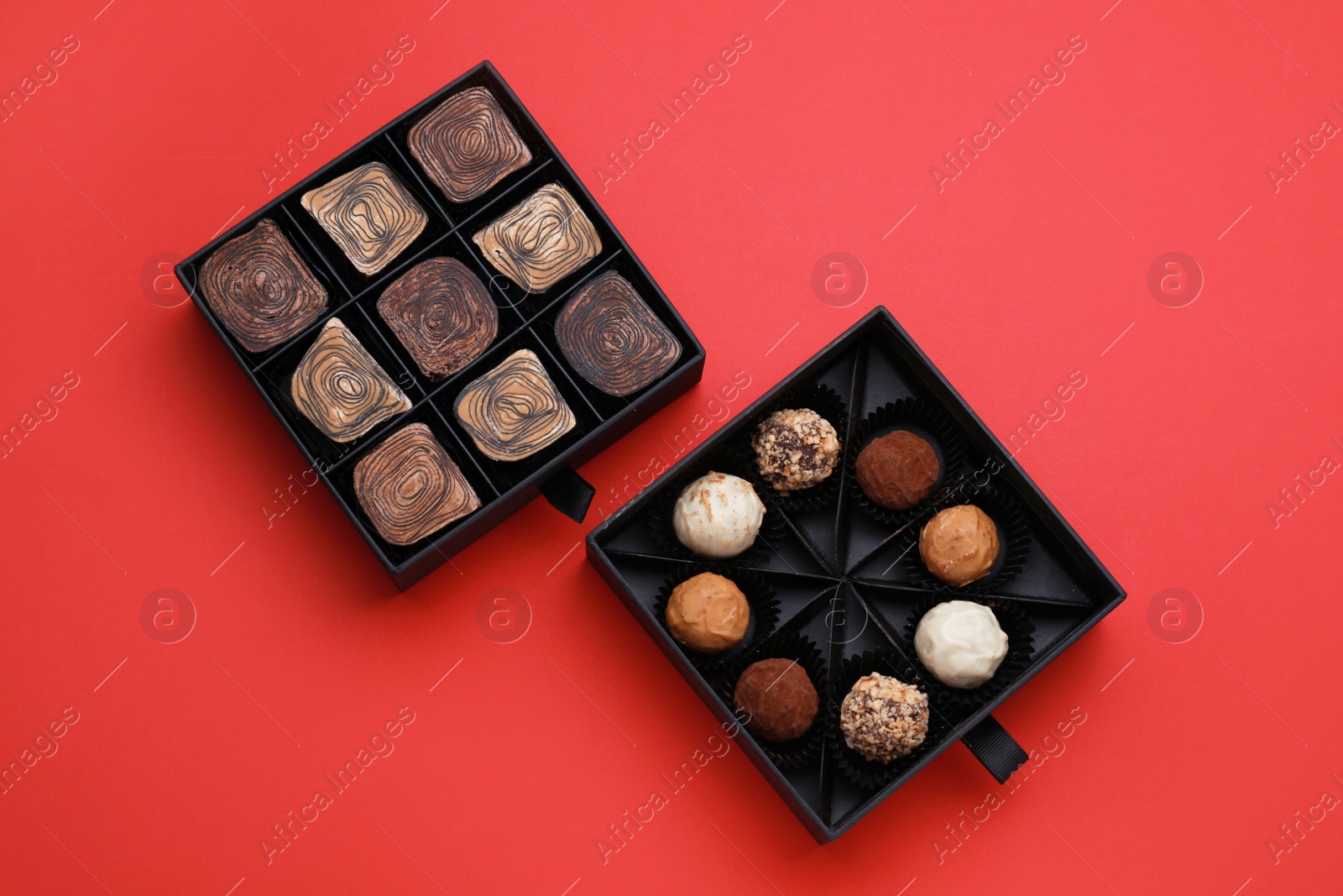 Photo of Boxes of tasty chocolate candies on red background, flat lay