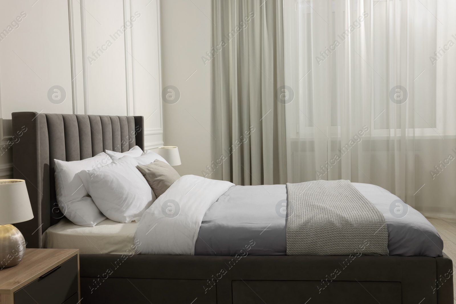 Photo of Comfortable bed near bedside table with lamp at home. Interior design