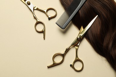 Photo of Professional scissors and comb with brown hair strand on beige background, flat lay