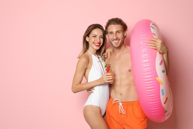 Photo of Happy young couple in beachwear with inflatable ring and cocktail on color background. Space for text