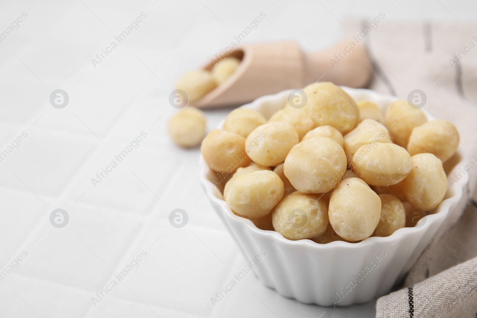 Photo of Tasty peeled Macadamia nuts in bowl on white tiled table, closeup