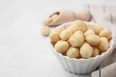 Tasty peeled Macadamia nuts in bowl on white tiled table, closeup