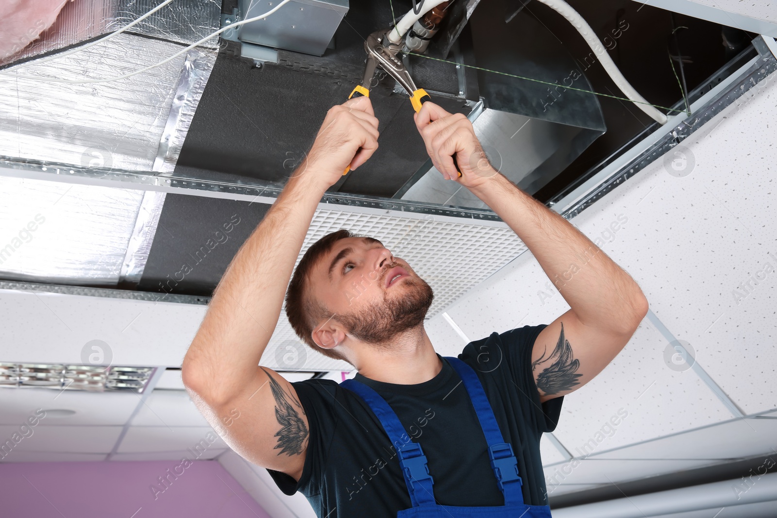 Photo of Young male technician repairing air conditioner indoors