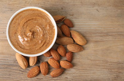 Delicious nut butter in bowl and almonds on wooden table, top view