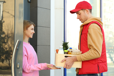 Photo of Woman receiving fresh products from courier at entrance. Food delivery service