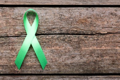 World Mental Health Day. Green ribbon on wooden background, top view with space for text