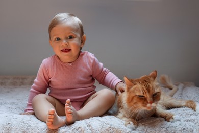 Photo of Adorable baby and cute red cat on bed indoors