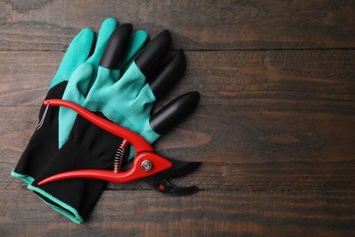 Photo of Pair of claw gardening gloves and secateurs on wooden table, top view. Space for text