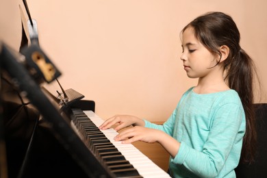 Photo of Cute little girl playing piano near beige wall. Music lesson
