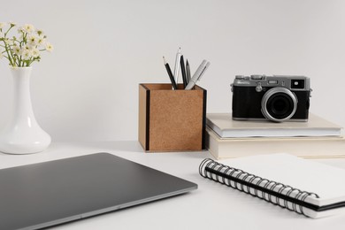 Photo of Home office. Laptop, vintage camera, flowers and stationery on white desk indoors