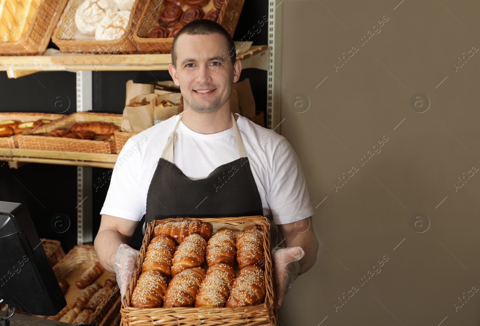 Photo of Portrait of professional baker holding tray with fresh buns near showcase in store