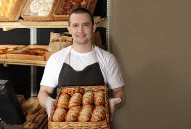 Photo of Portrait of professional baker holding tray with fresh buns near showcase in store