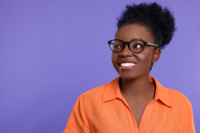 Portrait of happy young woman in eyeglasses on purple background. Space for text