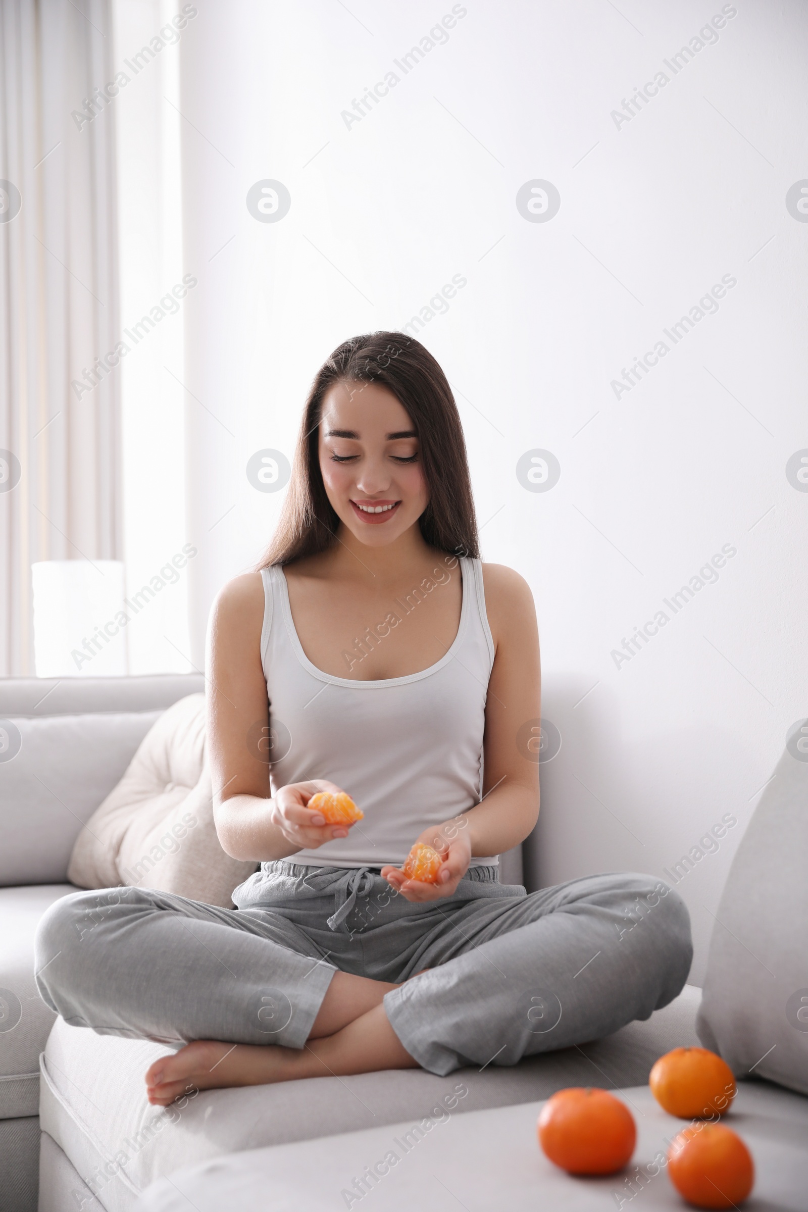 Photo of Young woman with peeled ripe tangerine on sofa at home