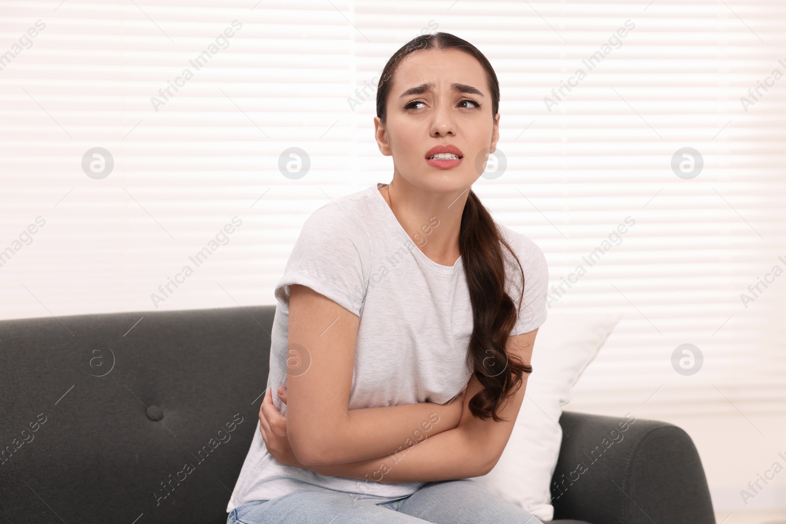 Photo of Woman suffering from abdominal pain on sofa at home. Unhealthy stomach