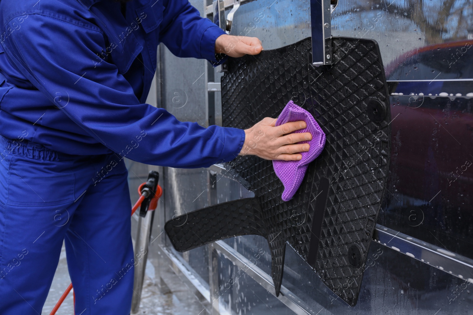 Photo of Worker wiping automobile floor mat at car wash, closeup