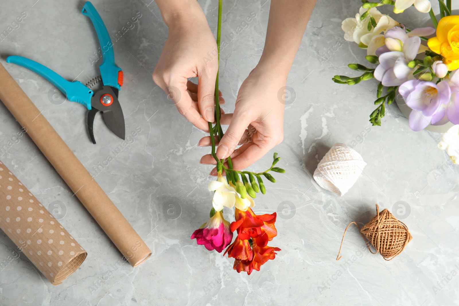 Photo of Woman making bouquet of freesia flowers at table, top view