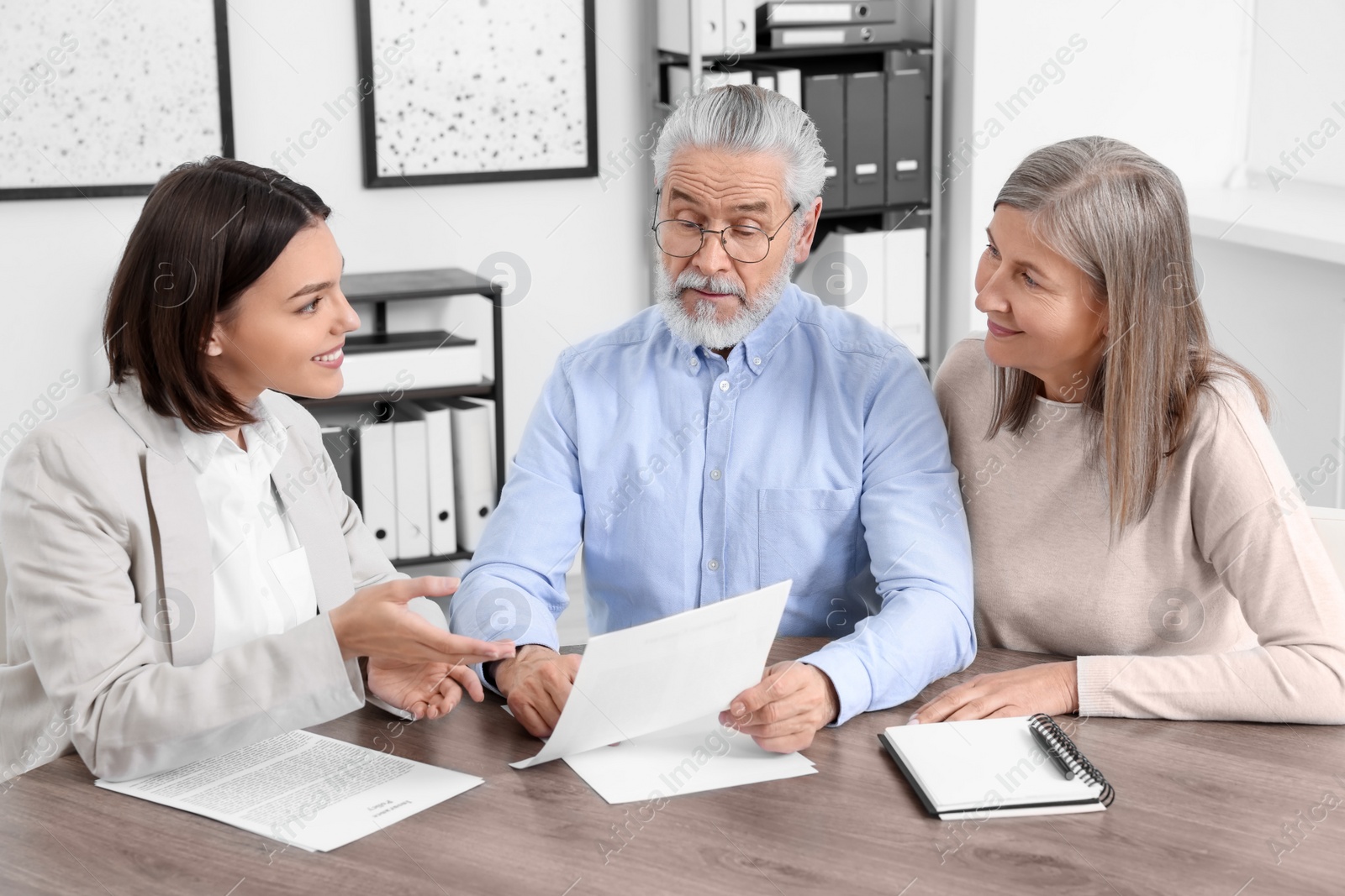 Photo of Elderly couple consulting insurance agent about pension plan at wooden table indoors