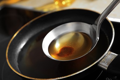 Photo of Ladle with used cooking oil over frying pan on stove, closeup