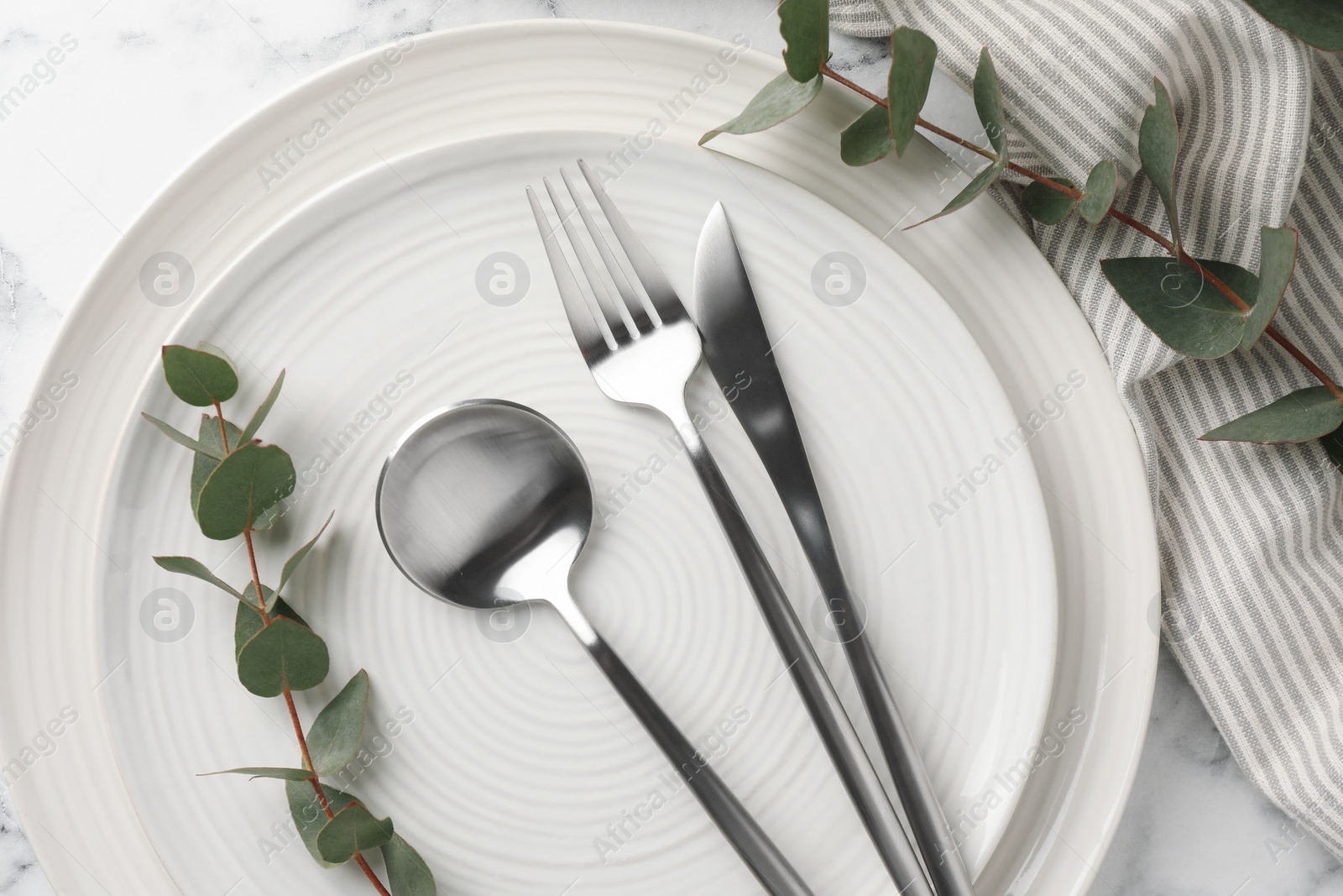 Photo of Stylish setting with cutlery, napkin, eucalyptus branches and plates on white marble table, top view