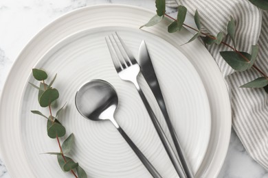 Photo of Stylish setting with cutlery, napkin, eucalyptus branches and plates on white marble table, top view