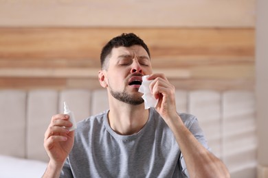 Photo of Sick man with nasal spray and paper tissue at home